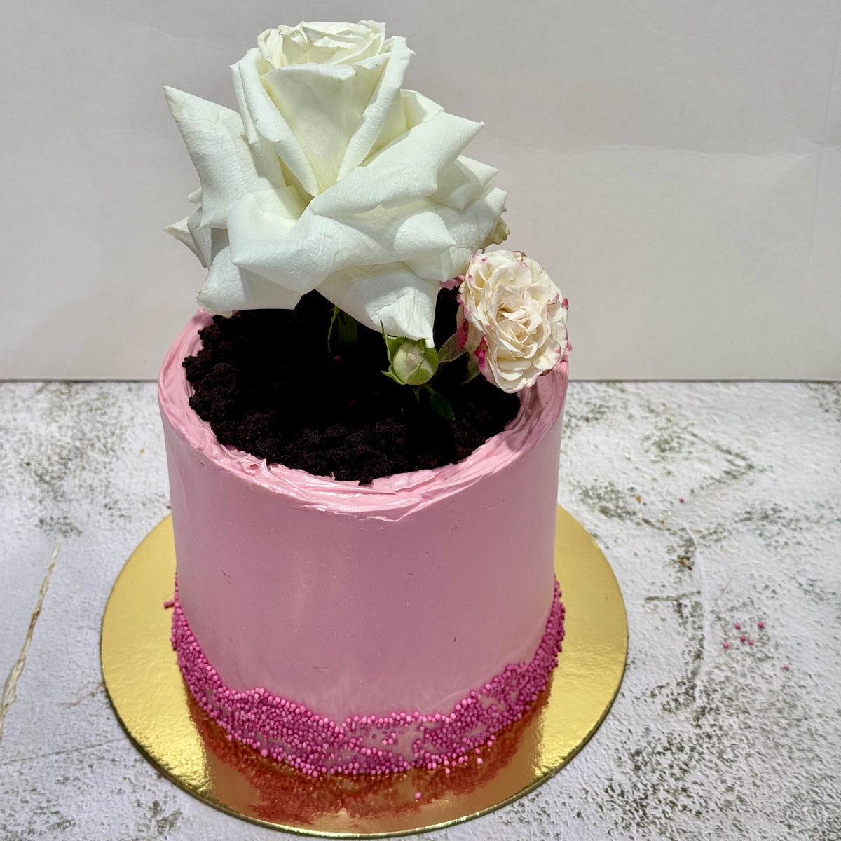 Pink round Mother’s Day Bloom Cake with fresh white rose and chocolate crumb soil