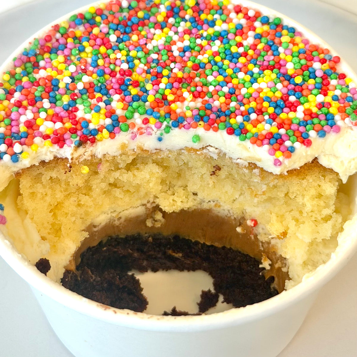 Dot Cake showing layers of vanilla sponge, dulce de leche, chocolate sponge and vanilla buttercream topped with colourful hundreds and thousands