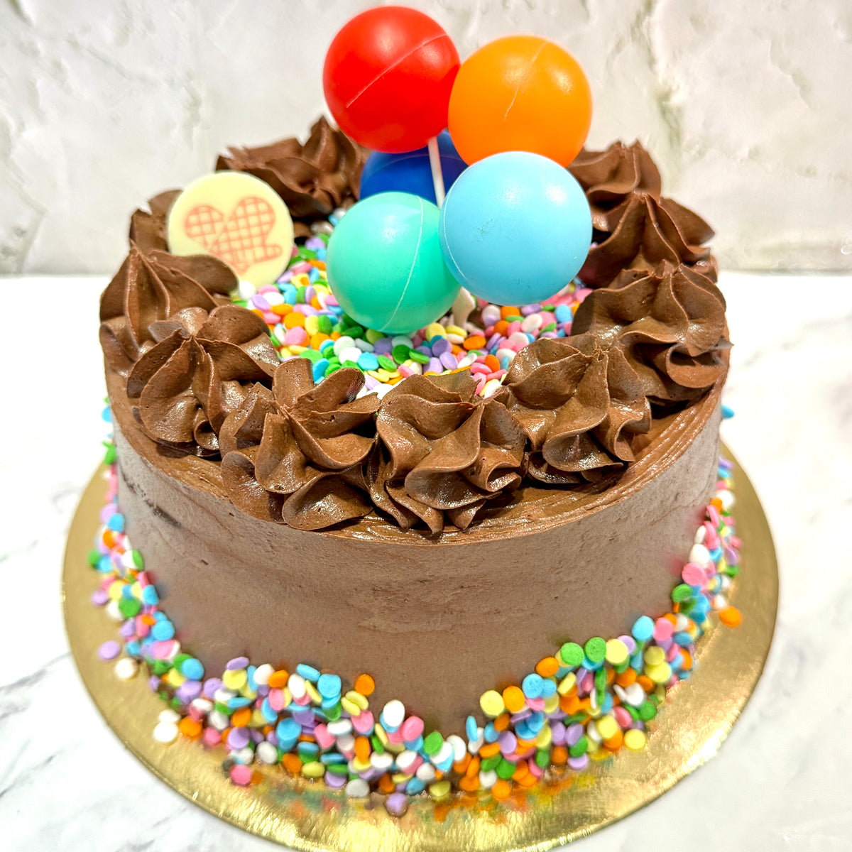 Chocolate cake with colorful sprinkles and balloons on a white background